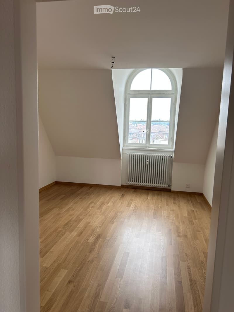 Empty room with wooden flooring, light-colored walls, and a large arched window with a radiator below it.