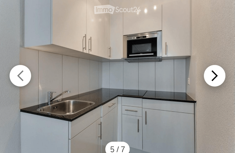 Modern kitchen with white cabinets, stainless steel sink, and microwave. Dark countertops and sleek design.