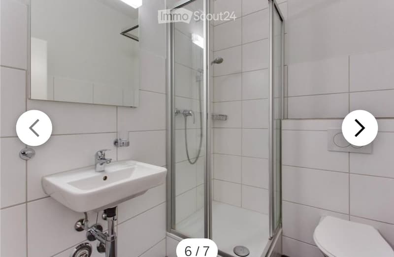 Modern bathroom with white tiles, a glass-enclosed shower, a sink with a mirror, and a toilet.