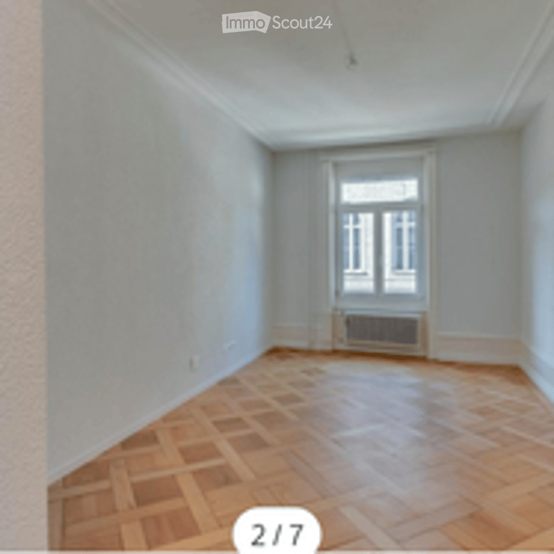 Completely empty room with wooden parquet flooring, white walls, and a single window with a radiator below it.