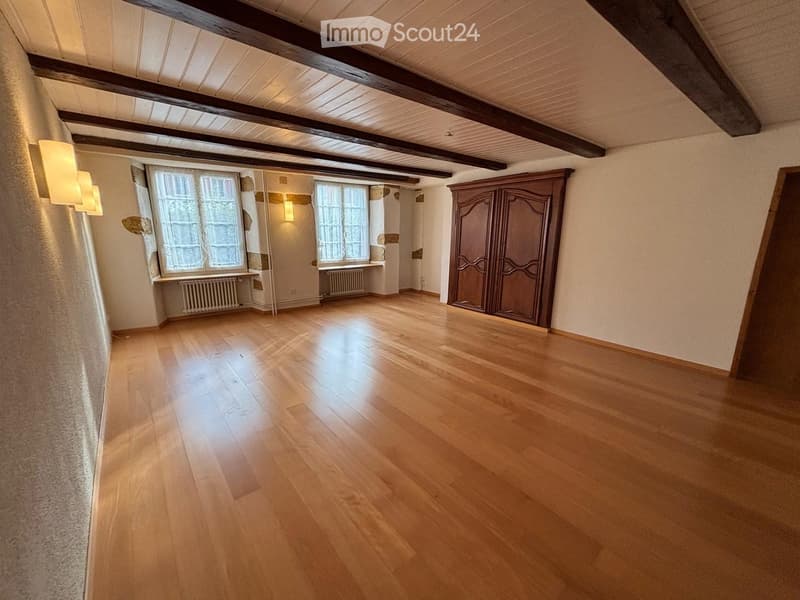 Empty room with wooden flooring, exposed wooden beams on the ceiling, large windows, and a built-in wardrobe.