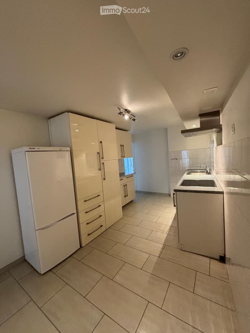 Modern kitchen with white cabinets, a refrigerator, and a sink area. The space features tiled flooring and recessed lighting.