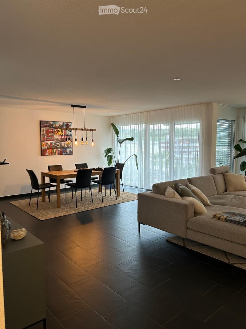 {"visible_features": ["Balcony / Terrace"],"type": "Living room and dining room","description": "The image shows an open-plan living and dining area. The living room has a large beige sofa, and the dining area has a wooden table with black chairs. The roo