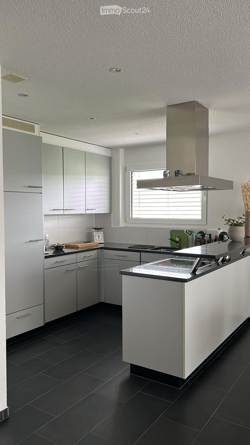Modern kitchen with gray cabinets, stainless steel appliances, black countertops, and a window above the sink.
