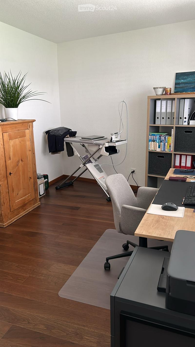 {"visible_features":[],"type":"Home office","description":"The image shows a home office space with a wooden desk, a computer, a printer, and a bookshelf. There is also an ironing board set up in the corner, indicating this space is used for both work and