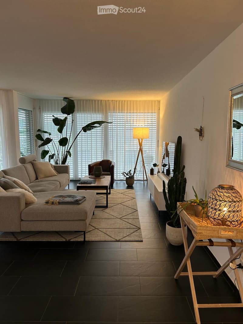 {"visible_features": ["Balcony / Terrace"],"type": "Living room","description": "Spacious living room with large windows, beige sofa, coffee table, floor lamp, and various decorative plants and accents. The room has a cozy and modern feel with a neutral c