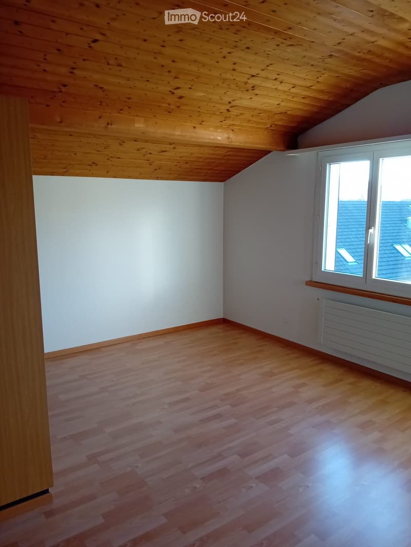 Empty room with wooden flooring, white walls, and a large window with a radiator below it.