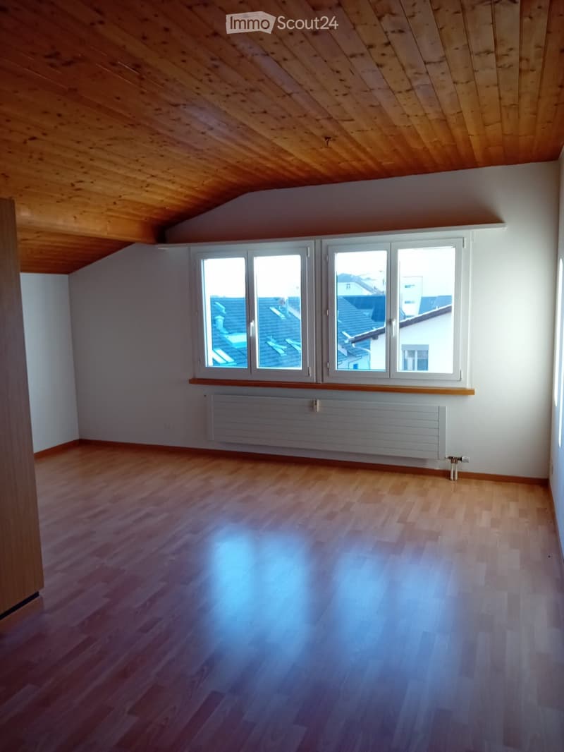 Empty room with wooden flooring, white walls, large windows, and a radiator. No furniture or equipment present.