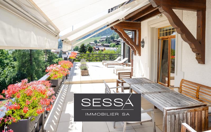 Balcony with wooden furniture, lounge chairs, potted plants, and a scenic mountain view.