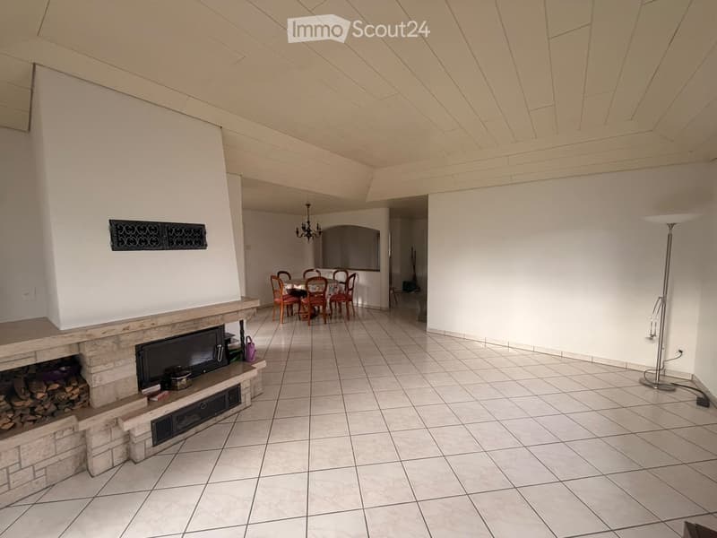 Living room with a stone fireplace, television, dining area with table and chairs, and a floor lamp.