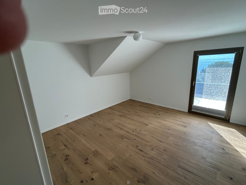 Empty room with wooden flooring, white walls, and a large window with a view of greenery outside.