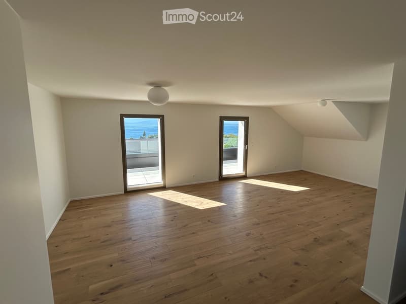 Empty room with wooden flooring, white walls, and two large glass doors leading to a balcony with ocean views.