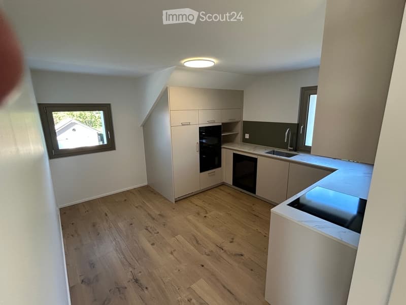 Modern kitchen with light-colored cabinets, wooden flooring, and a sleek countertop. Features include an integrated oven, sink, and faucet.