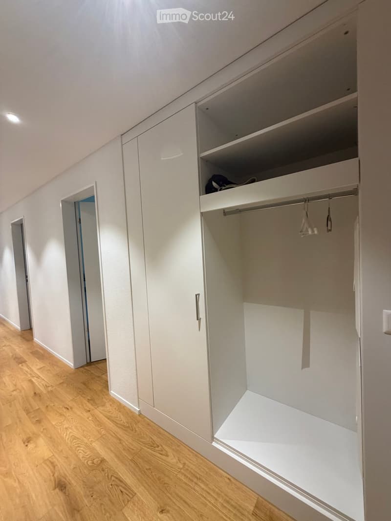 Empty closet with white built-in cabinets and wooden flooring, featuring a partially open door revealing a small hallway.