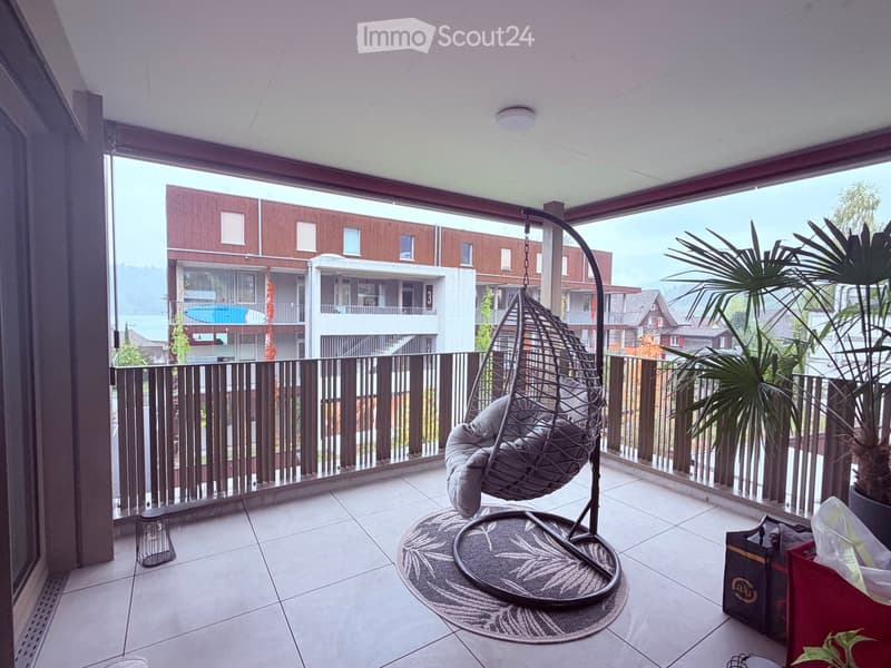 Balcony with a wicker hanging chair, a round rug, a potted plant, and a handbag placed on the floor.