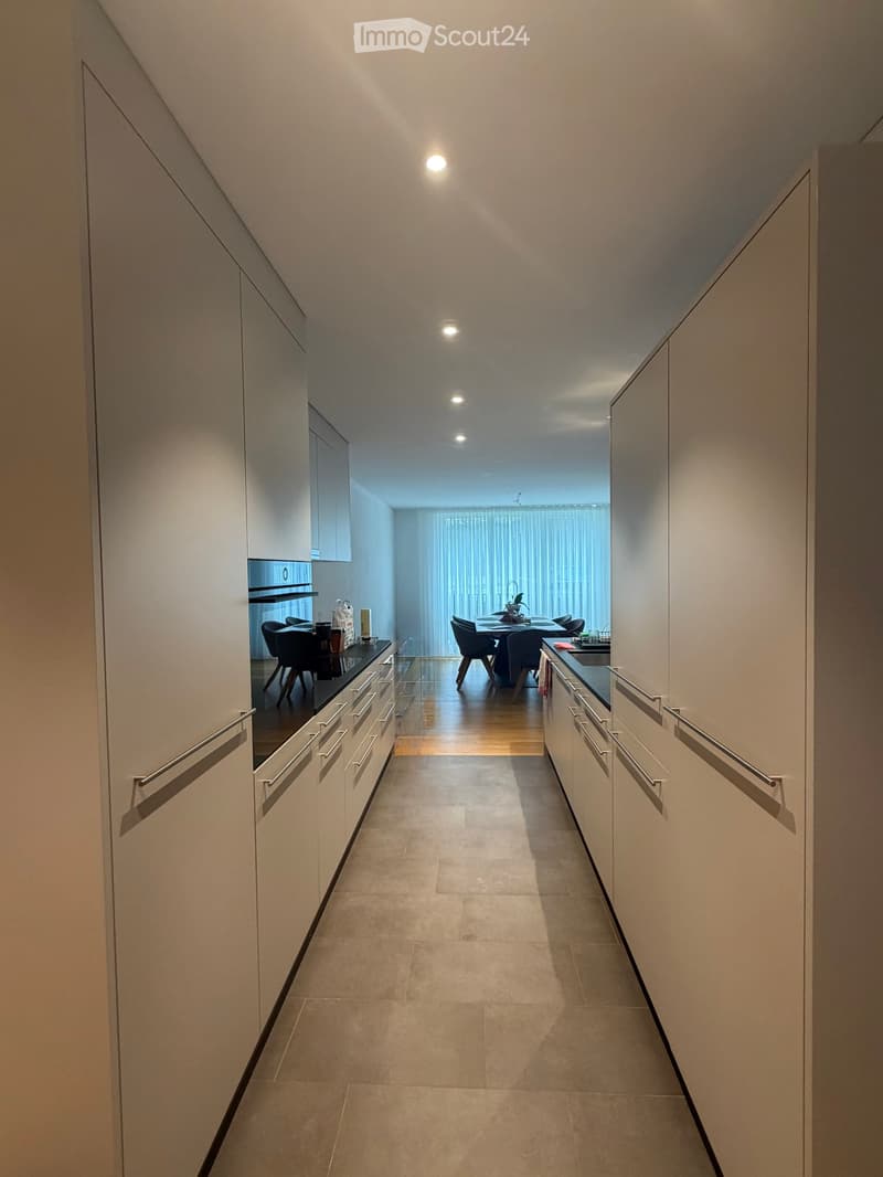 Modern hallway with sleek white cabinets, recessed lighting, and a view into a dining area with a table and chairs.
