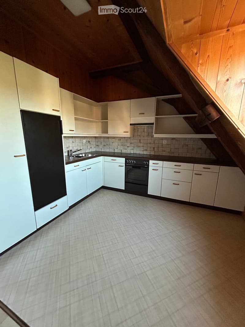 Modern kitchen with white cabinets, black countertop, and stainless steel sink and oven. The space features a slanted wooden ceiling and tiled backsplash.