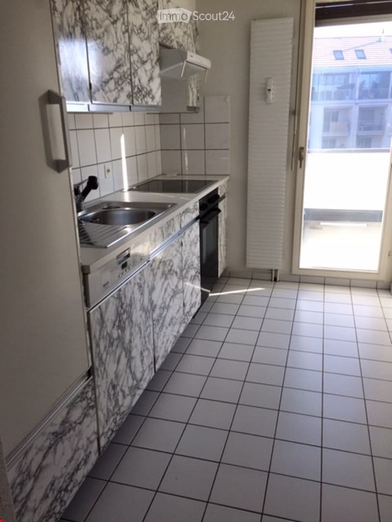 Modern kitchen with marble-patterned cabinets, stainless steel sink, oven, and dishwasher. White tiled floor and walls, large window with view.