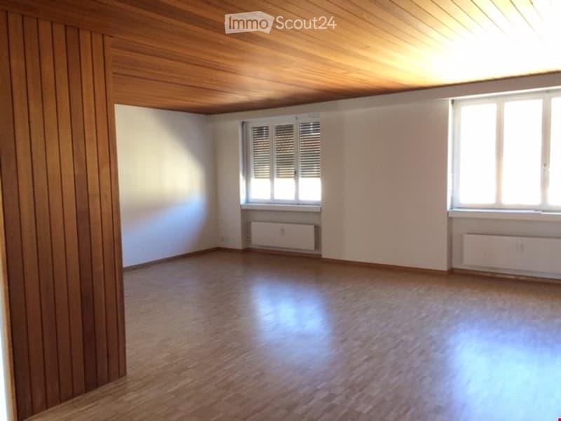 Empty room with wooden flooring, white walls, and wooden ceiling. Two windows with blinds and radiators below them.