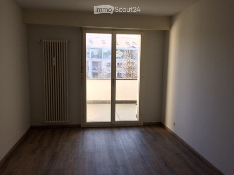 Empty room with wooden flooring, white walls, and a large sliding glass door leading to a balcony.