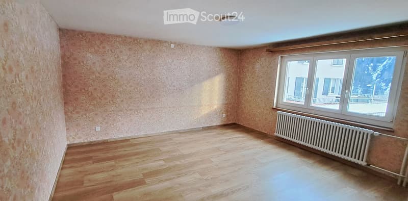 Empty room with wooden flooring, patterned walls, and a large window with a radiator below it.