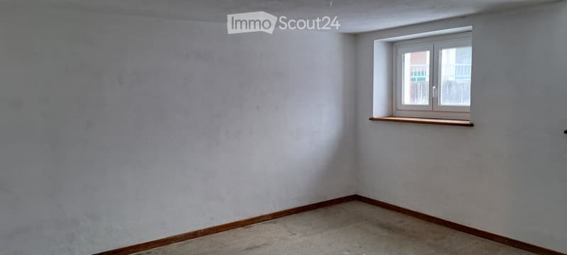 Empty room with light grey walls, wooden baseboards, and a single window with a small wooden shelf below it.