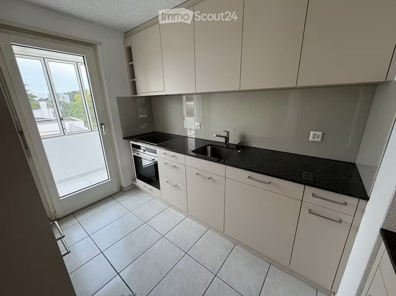 Modern kitchen with white cabinets, black countertops, and a large window offering a view of the outside area.