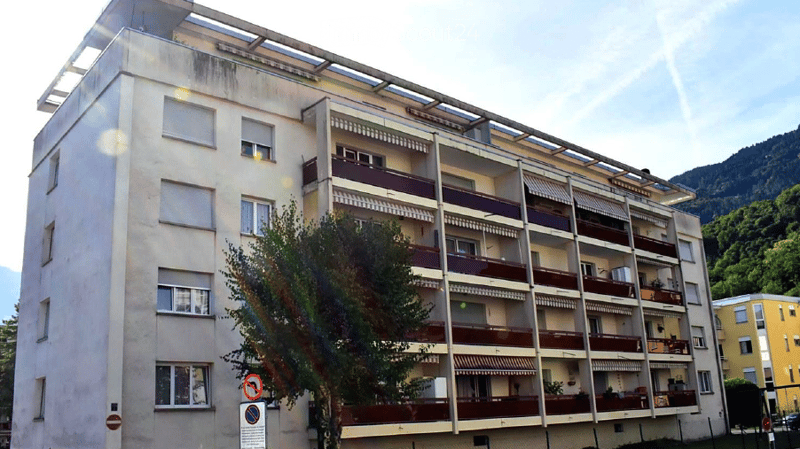 Multi-story apartment building with multiple balconies and a scenic mountain view in the background.