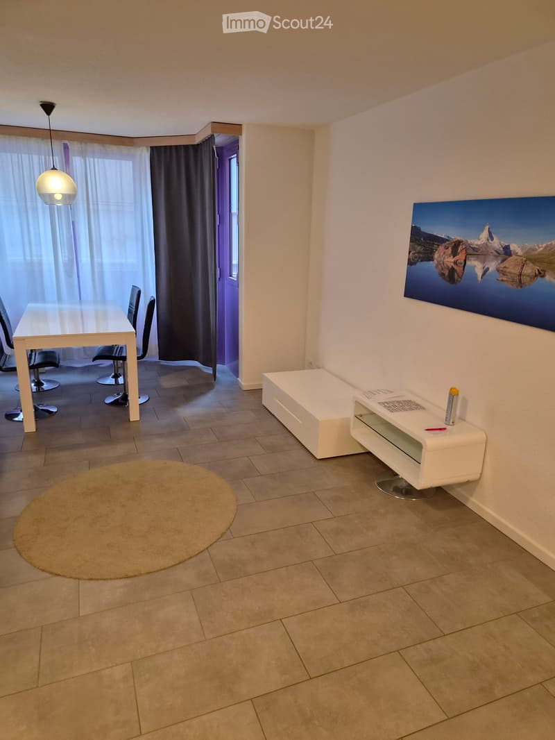 Modern furnished room with a white table, chairs, a round rug, a white cabinet, and a large picture frame on the wall. Natural light filters through sheer curtains.