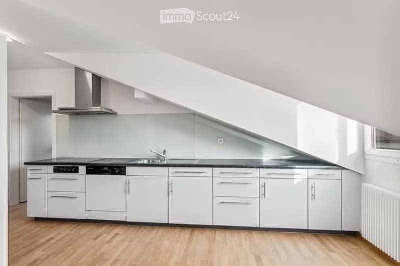 Modern, minimalist kitchen with white cabinets, black countertops, and a sleek stainless steel range hood. The space features a full-height window and a wooden floor.