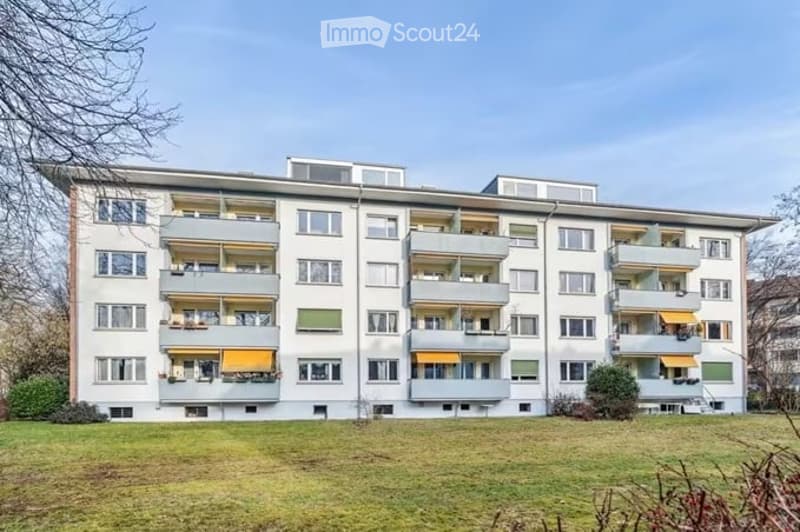 Multi-story residential building with multiple balconies and yellow awnings, surrounded by a grassy area.