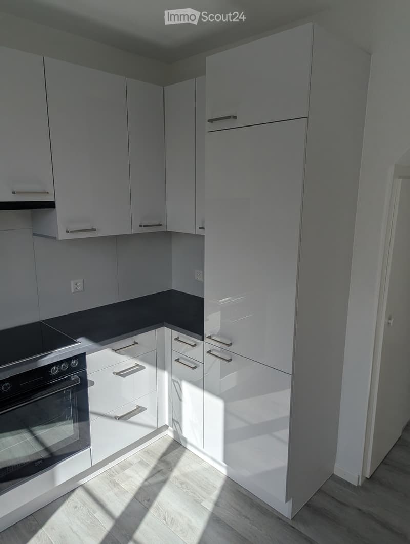 Modern kitchen with white cabinets, stainless steel oven, and light wooden flooring.