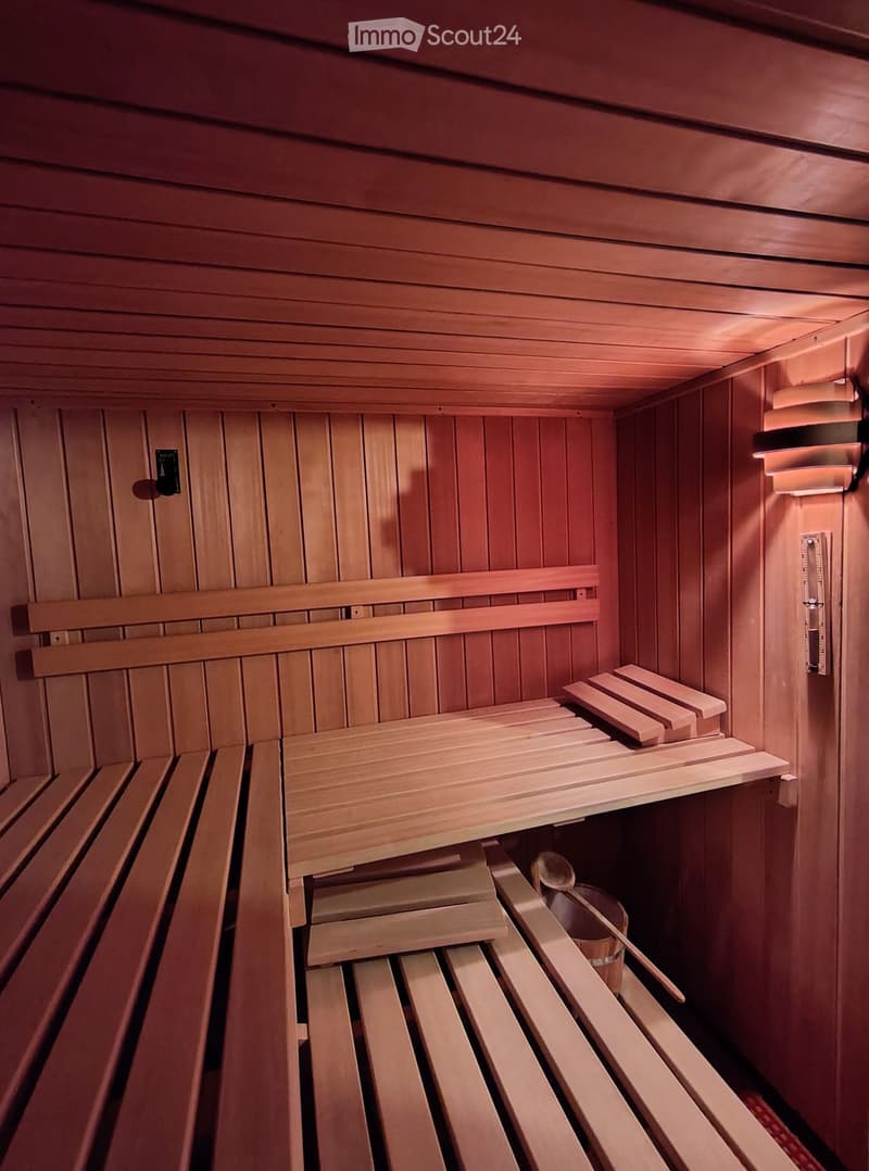 Wooden sauna interior with benches, shelves, and a bucket with a paddle.