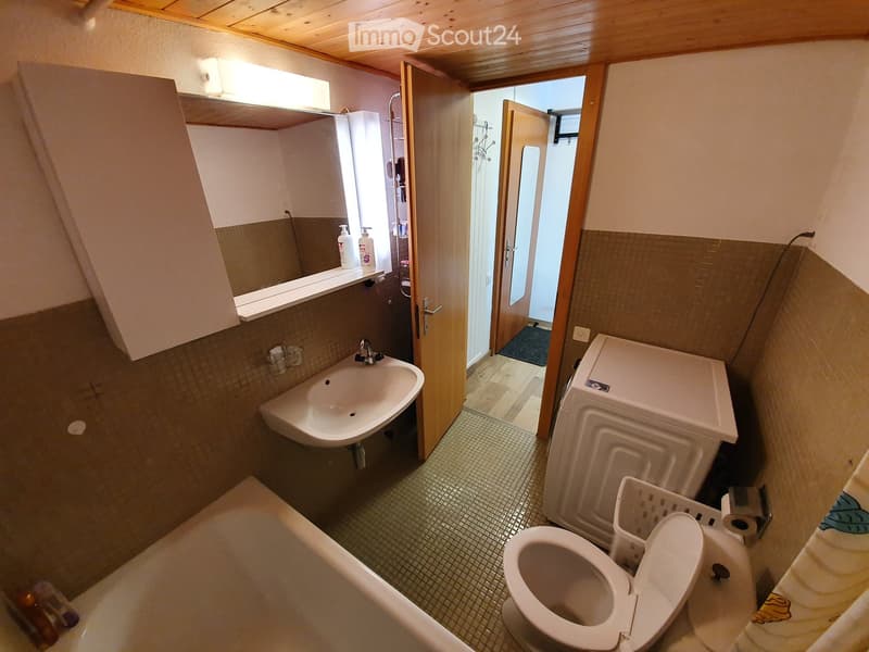 Bathroom with a sink, toilet, bathtub, mirror, and washing machine. The room has tiled walls and a wooden ceiling.