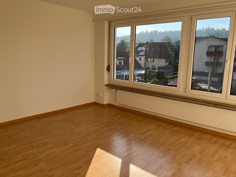 Empty room with wooden flooring, large windows offering a view of the neighborhood, and a radiator under the windows.