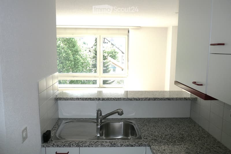Modern kitchen with granite countertops, stainless steel sink, and white tiled backsplash. Large windows provide natural light.