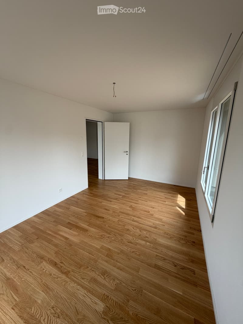Empty room with light wooden flooring and white walls, featuring a white door and a window with white frame.