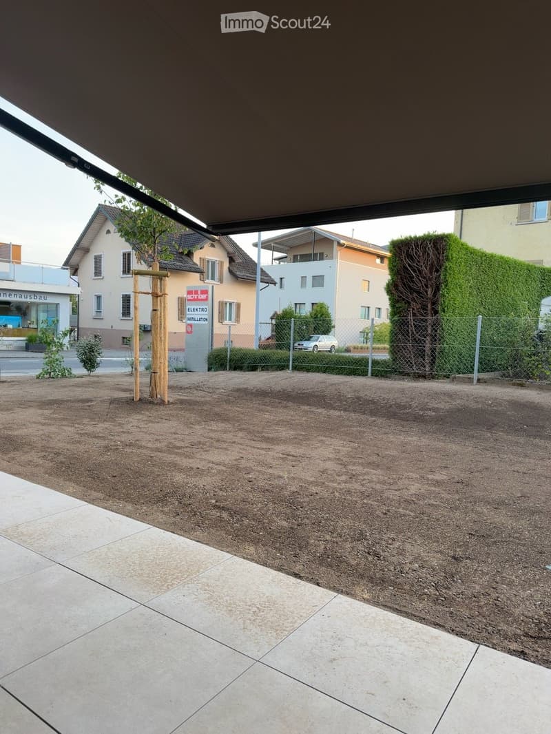 Garden area with gravel ground, small wooden structure, fence, and surrounding residential buildings.