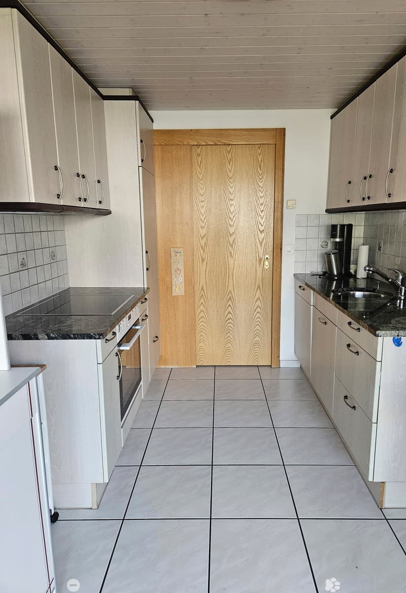 Modern kitchen with white cabinets, granite countertops, tiled backsplash, and a central door.