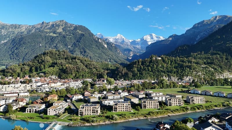 Aerial view of a town nestled in a valley surrounded by mountains, with a river running through it and various residential and commercial buildings.