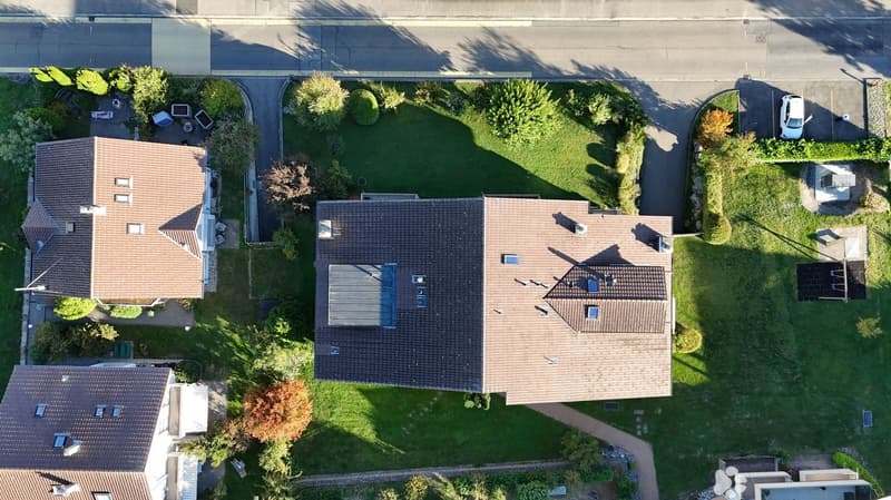 Aerial view of a residential area with multiple houses, well-maintained lawns, and surrounding greenery.