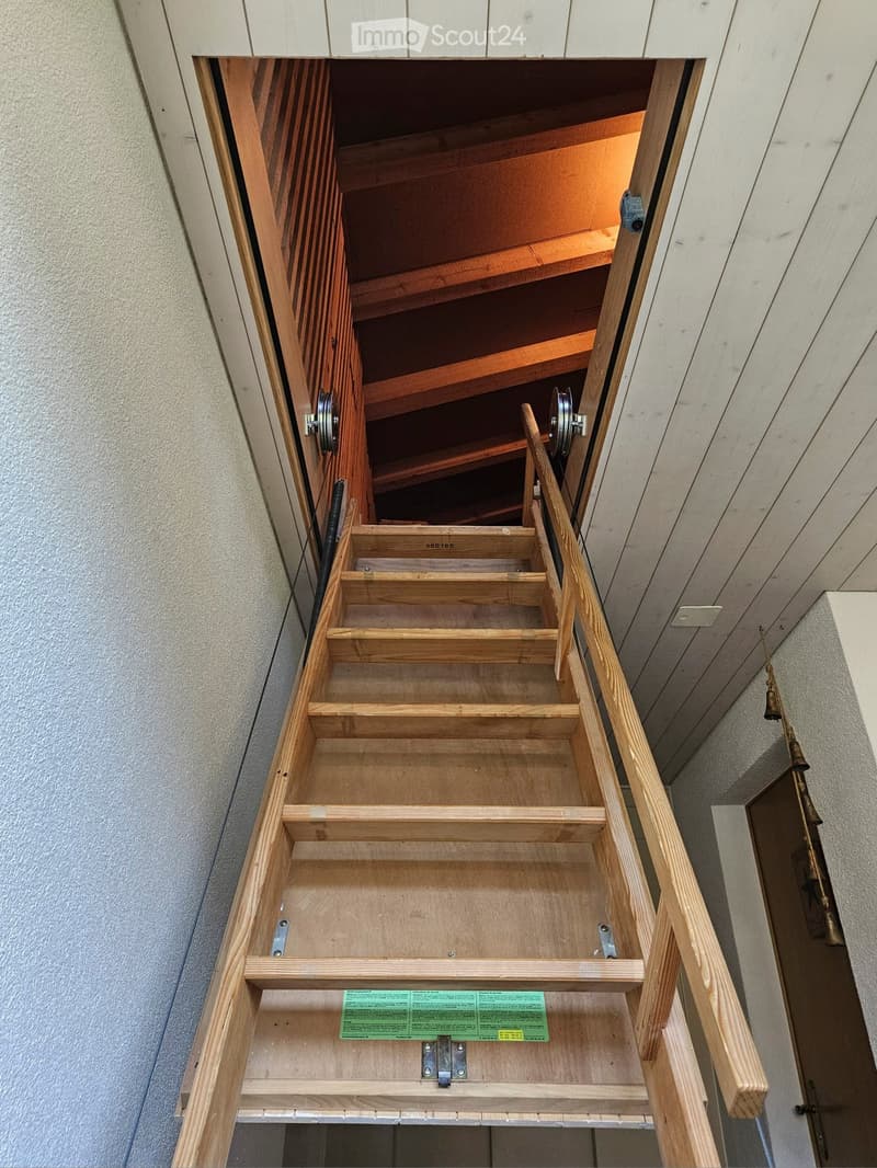 Wooden staircase with open wooden railings and visible wooden beams in the ceiling above.