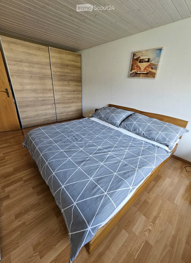 Cozy bedroom with a wooden bed, grey bedding, a large wardrobe, and a California-themed picture on the wall.