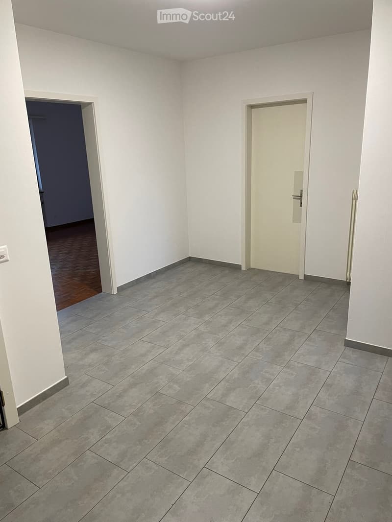 Empty room with grey tiled floor and white walls, featuring two doors and a visible electrical outlet.