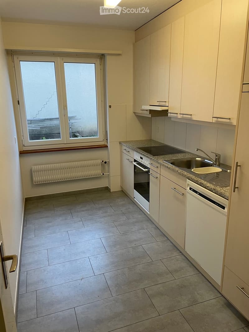 Modern kitchen with white cabinets, granite countertop, sink, faucet, oven, dishwasher, and radiator under window.