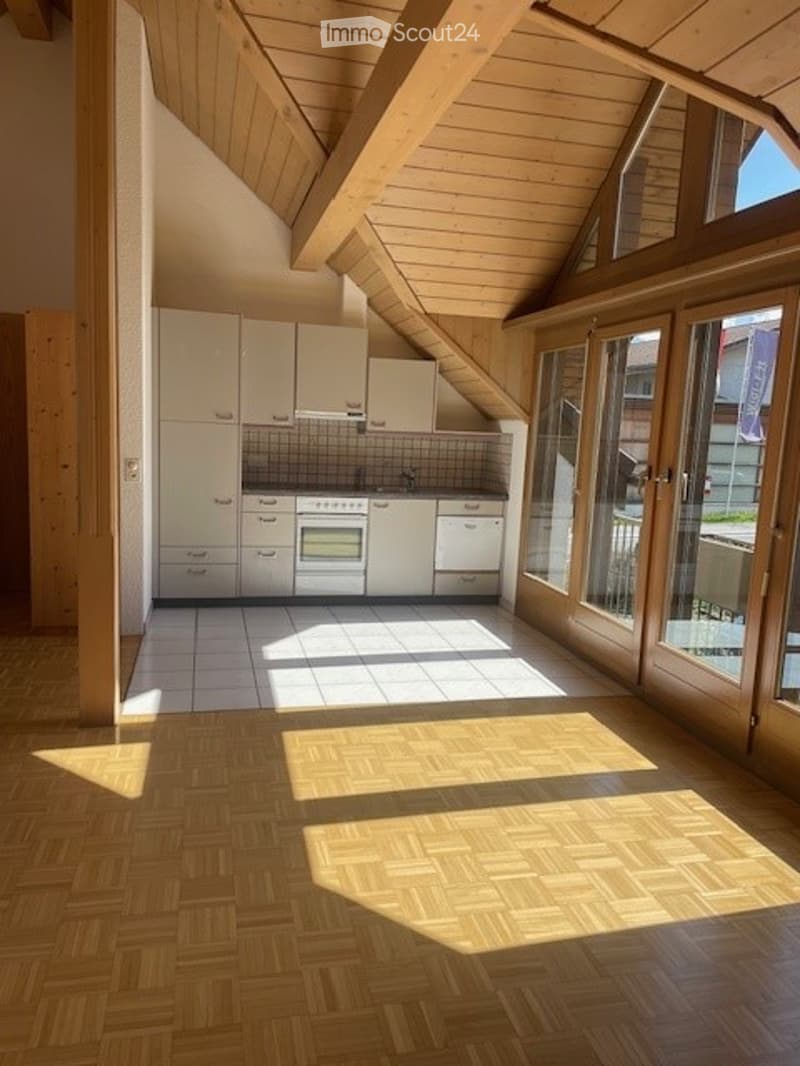 Bright kitchen with white cabinets, an oven, and a sink, featuring wooden beams on the ceiling and large windows allowing natural light to flood the space.