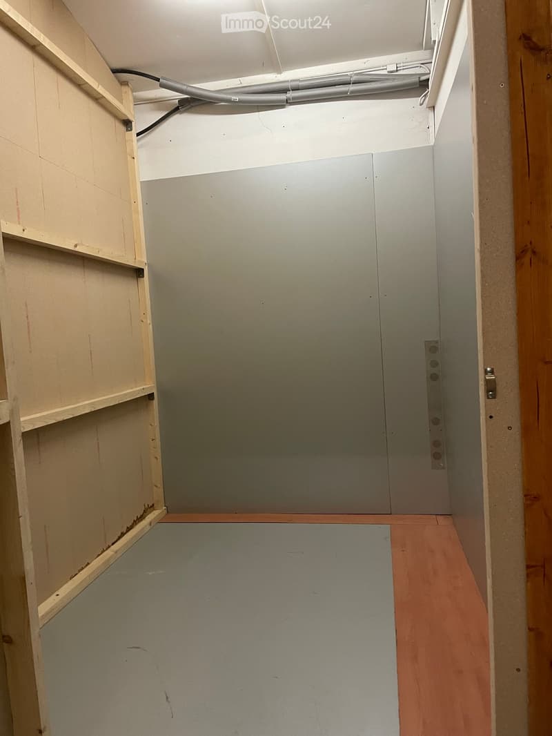 Empty room with unfinished walls and wooden floor, showing exposed wiring and construction materials.