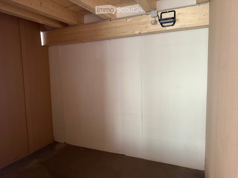 Empty room with white walls, wooden ceiling beams, and a dark floor. No furniture or equipment is present.