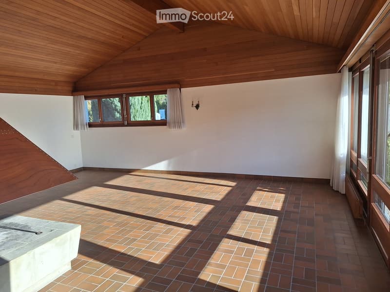 An unfurnished room with wooden ceiling, brick floor, large windows with curtains, and a wall-mounted light fixture.