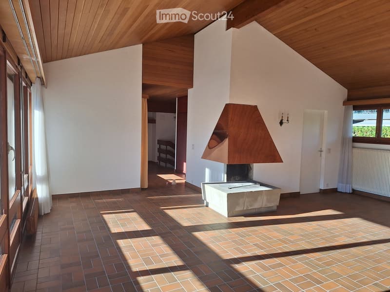 Bright living room with wooden ceiling, tiled floor, fireplace with wooden mantel, radiator, and a small shelf in the background.